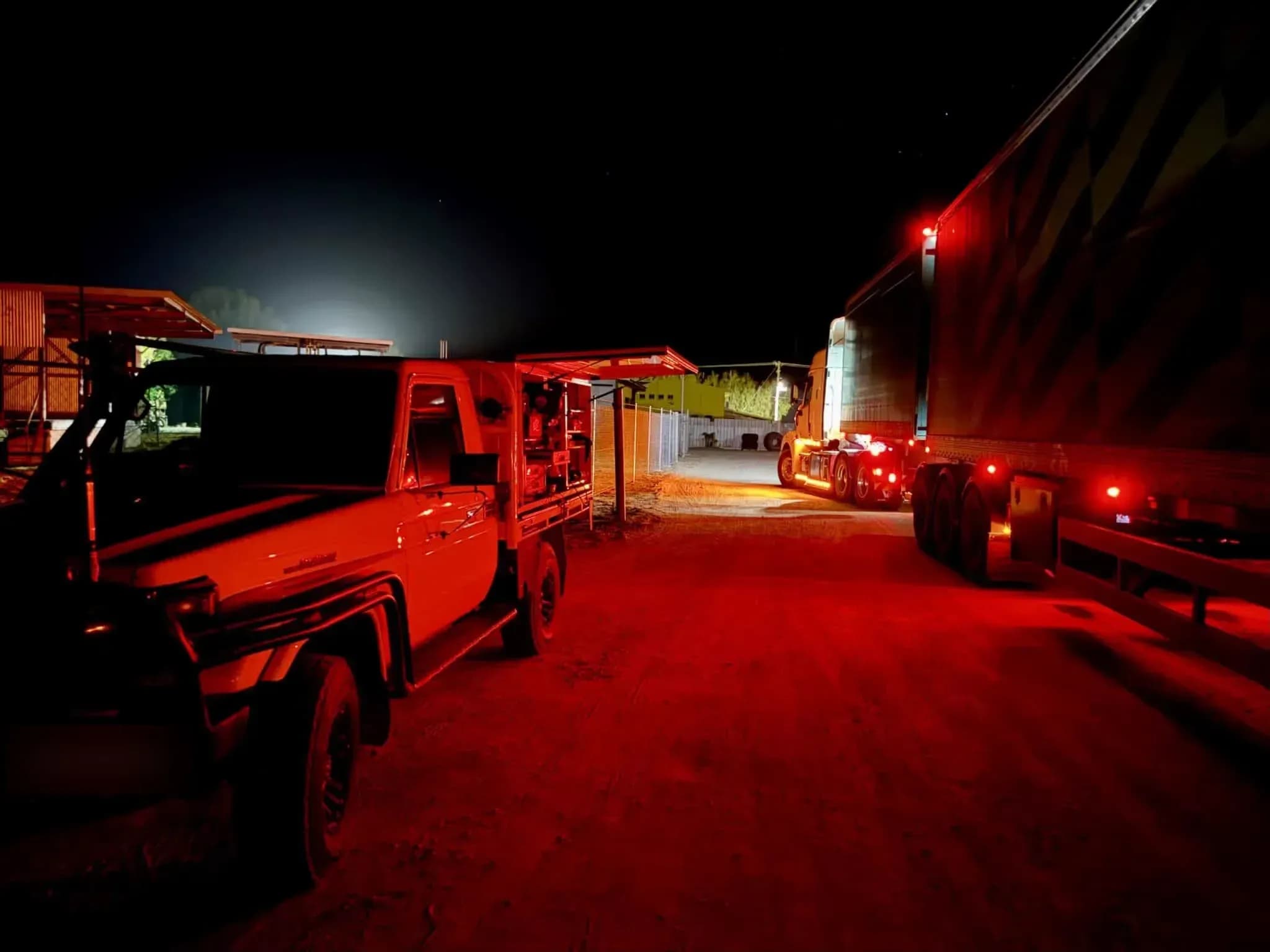 A Townlec service ute with its canopy open beside a truck and trailer at night, lit red